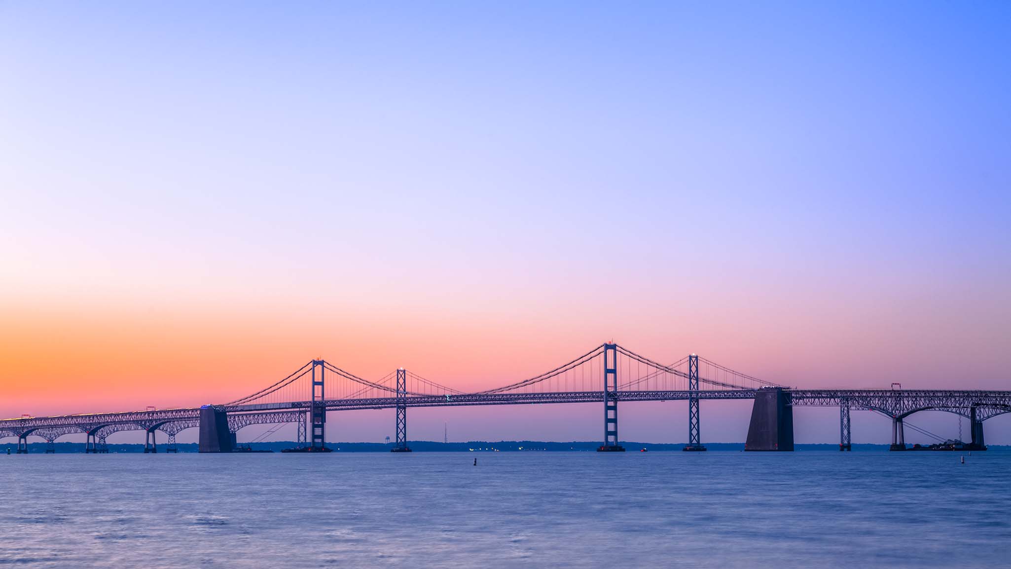 A beautiful sunrise over the calm waters under the Chesapeake Bay Bridge. The steel and concrete cantilever and suspension bridge near Baltimore, MD, stretches across the Chesapeake Bay.