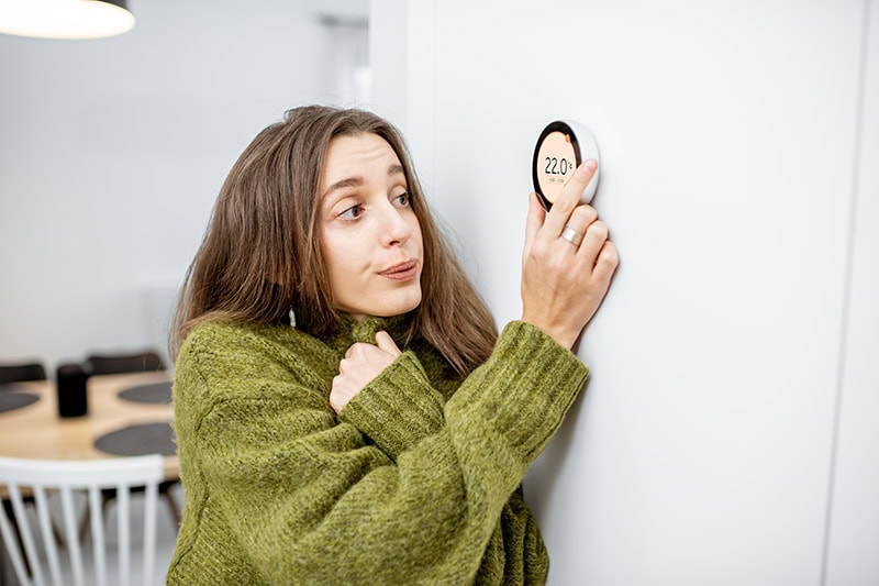 woman wearing sweater as she adjusts thermostat.